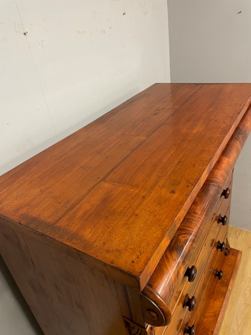 A 19th-century Scottish flame mahogany chest of drawers featuring a top cushion drawer, carved corbels, five lower drawers with turned wooden knobs, and turned feet. View IV