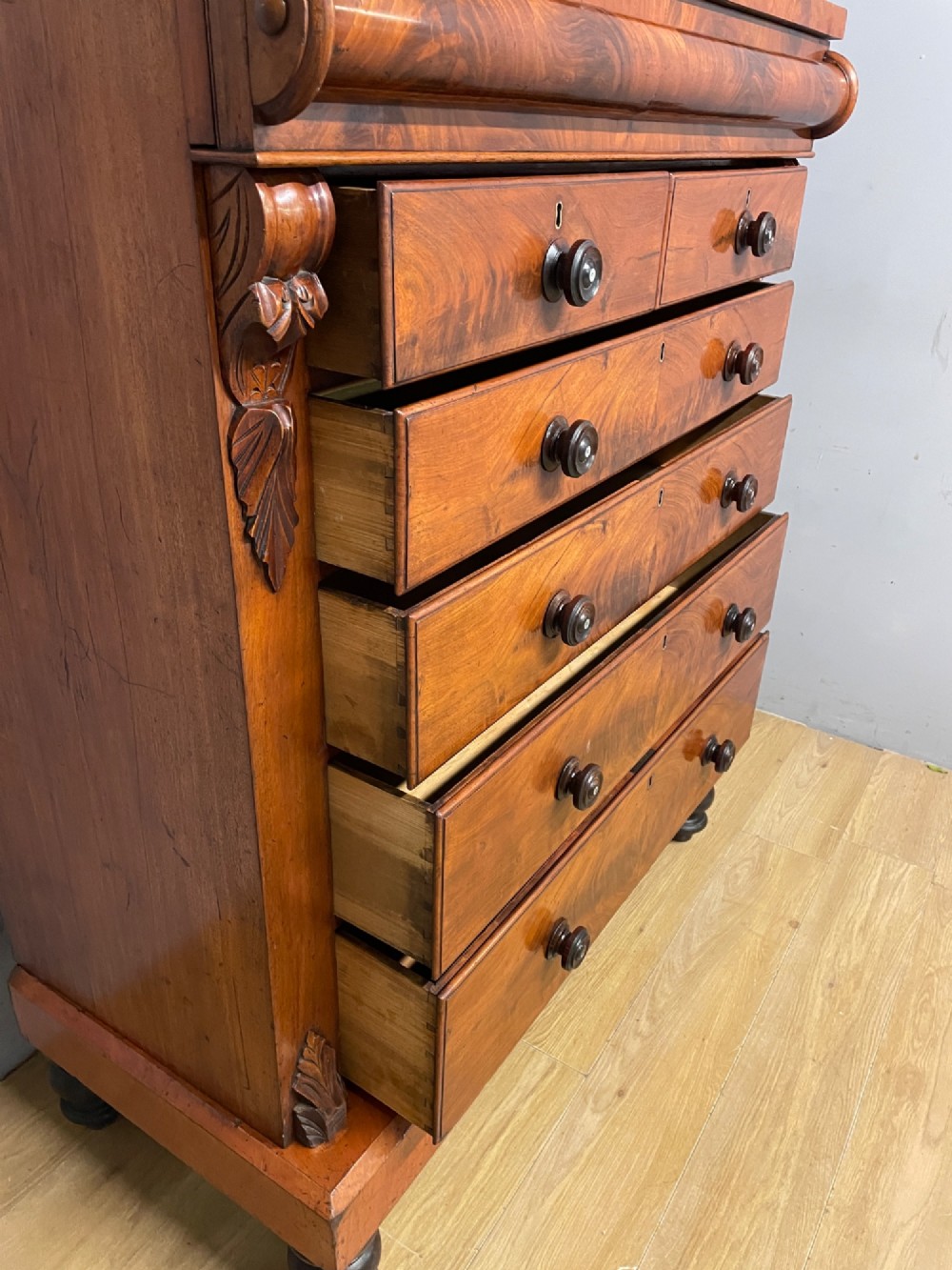 A 19th-century Scottish flame mahogany chest of drawers featuring a top cushion drawer, carved corbels, five lower drawers with turned wooden knobs, and turned feet. View VI