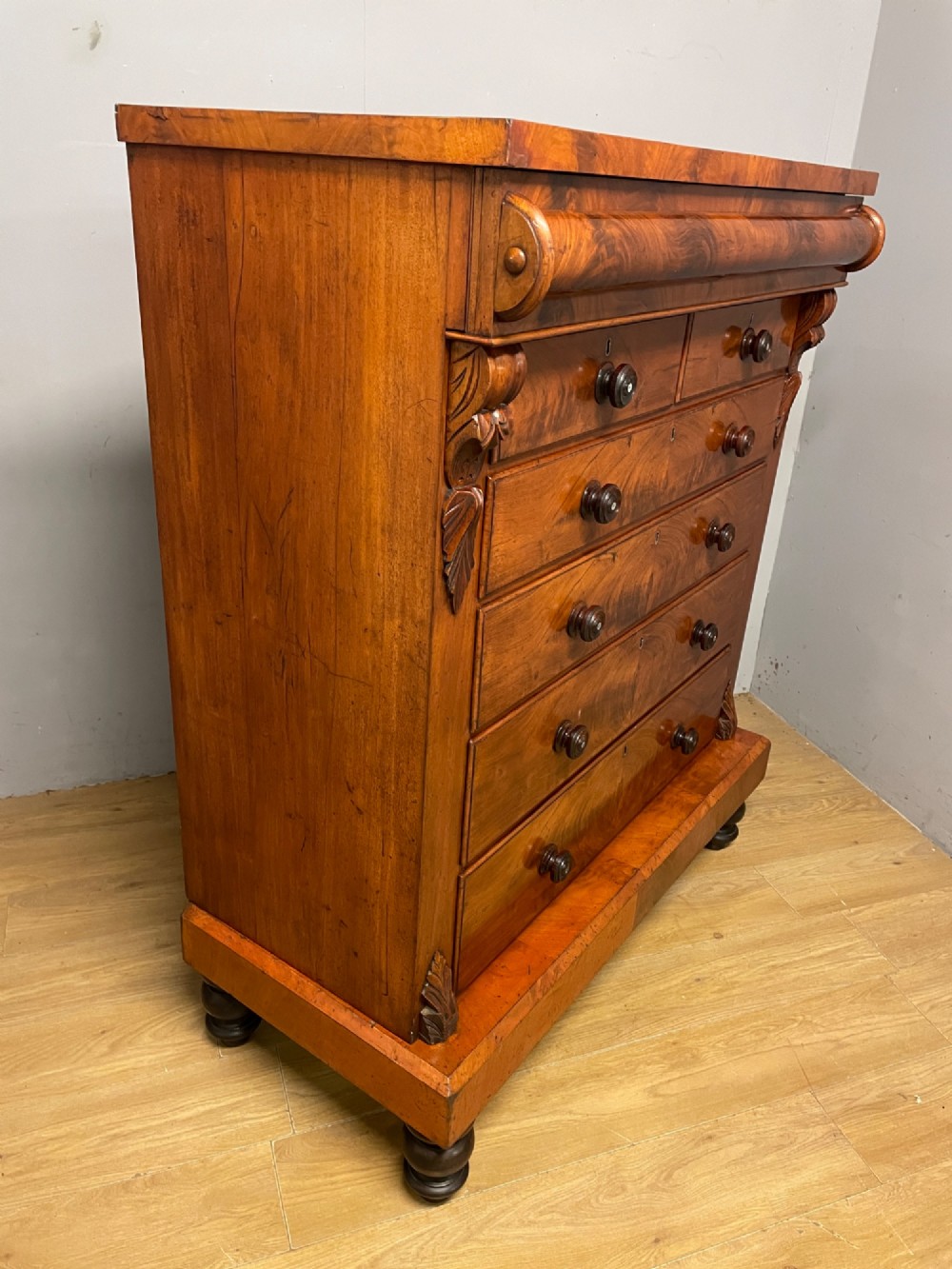 A 19th-century Scottish flame mahogany chest of drawers featuring a top cushion drawer, carved corbels, five lower drawers with turned wooden knobs, and turned feet. View VIII
