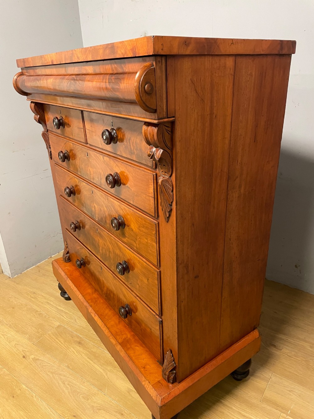 A 19th-century Scottish flame mahogany chest of drawers featuring a top cushion drawer, carved corbels, five lower drawers with turned wooden knobs, and turned feet. View IX