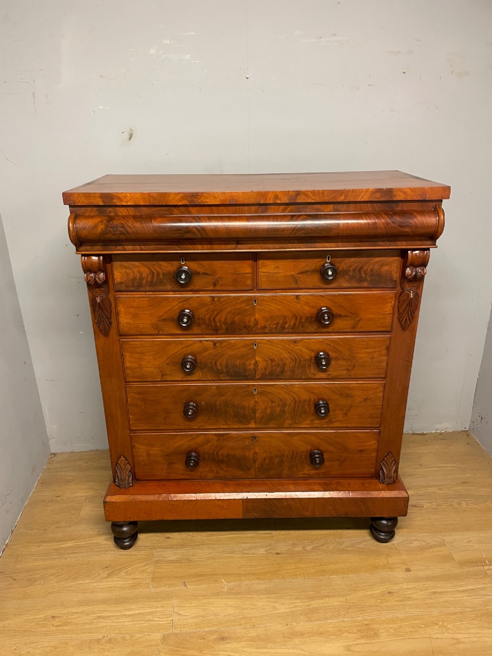 A 19th-century Scottish flame mahogany chest of drawers featuring a top cushion drawer, carved corbels, five lower drawers with turned wooden knobs, and turned feet. View XI