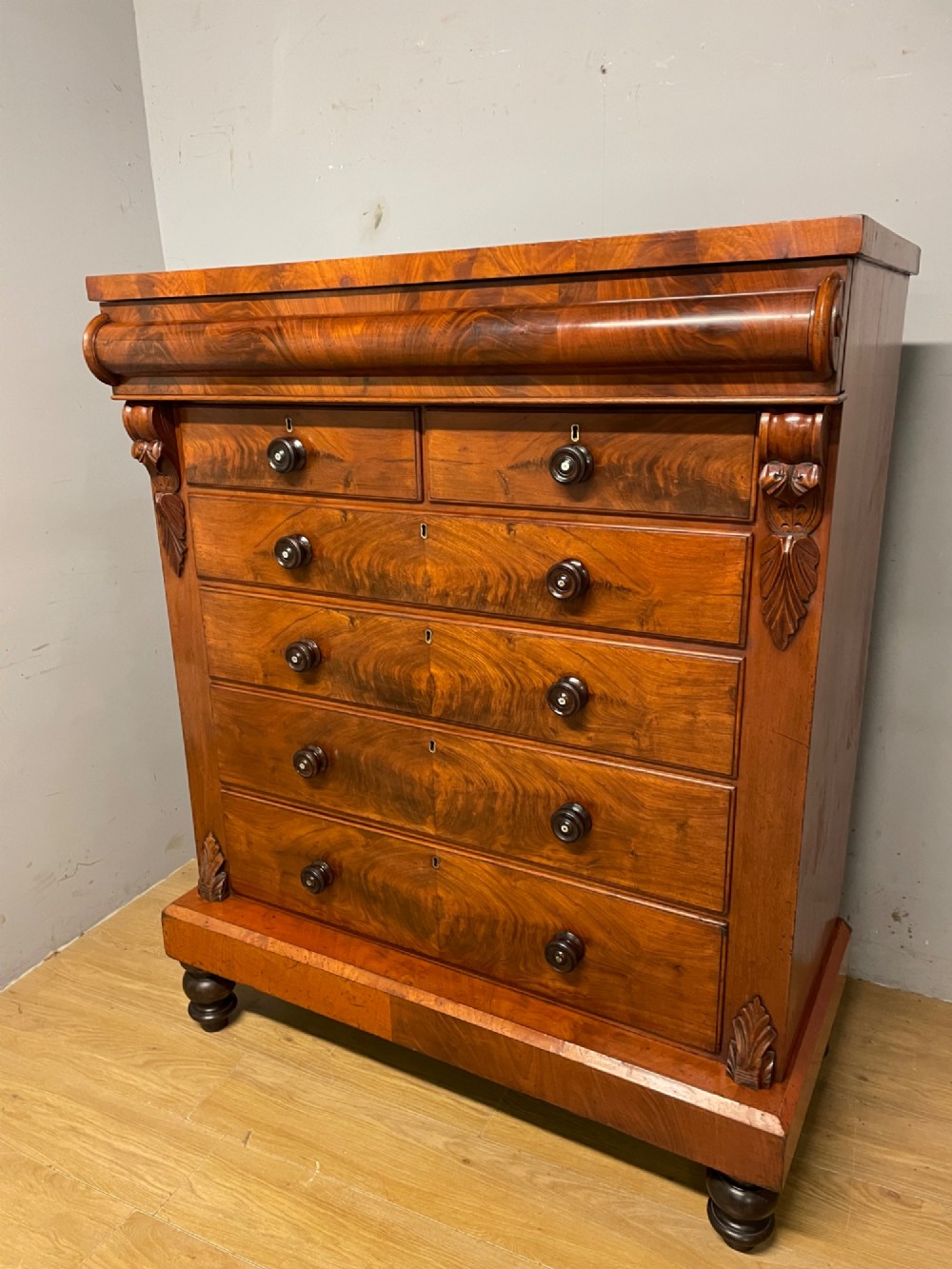 A 19th-century Scottish flame mahogany chest of drawers featuring a top cushion drawer, carved corbels, five lower drawers with turned wooden knobs, and turned feet. View XII