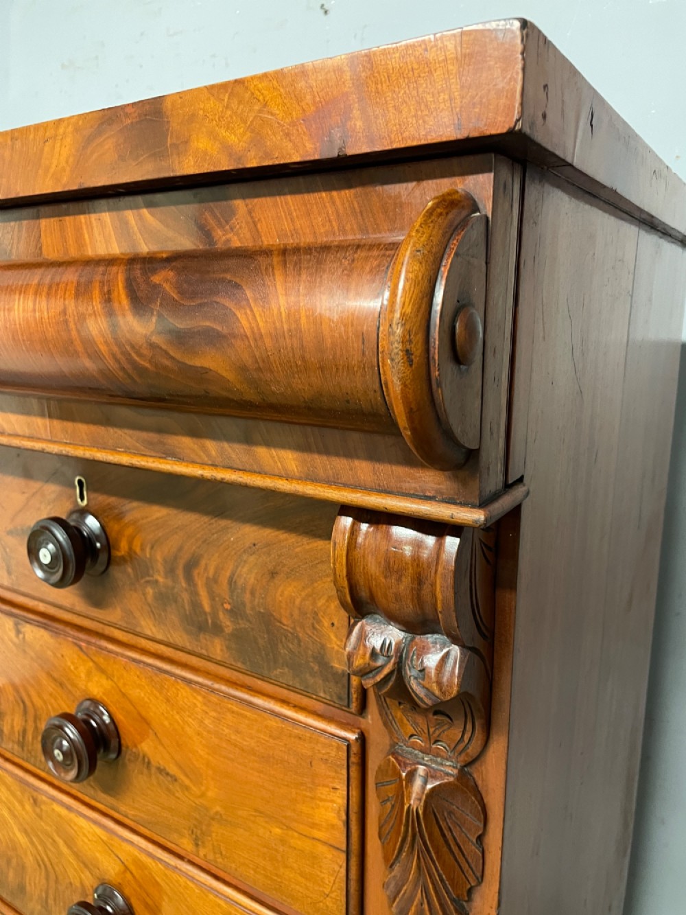 A 19th-century Scottish flame mahogany chest of drawers featuring a top cushion drawer, carved corbels, five lower drawers with turned wooden knobs, and turned feet. View XIII