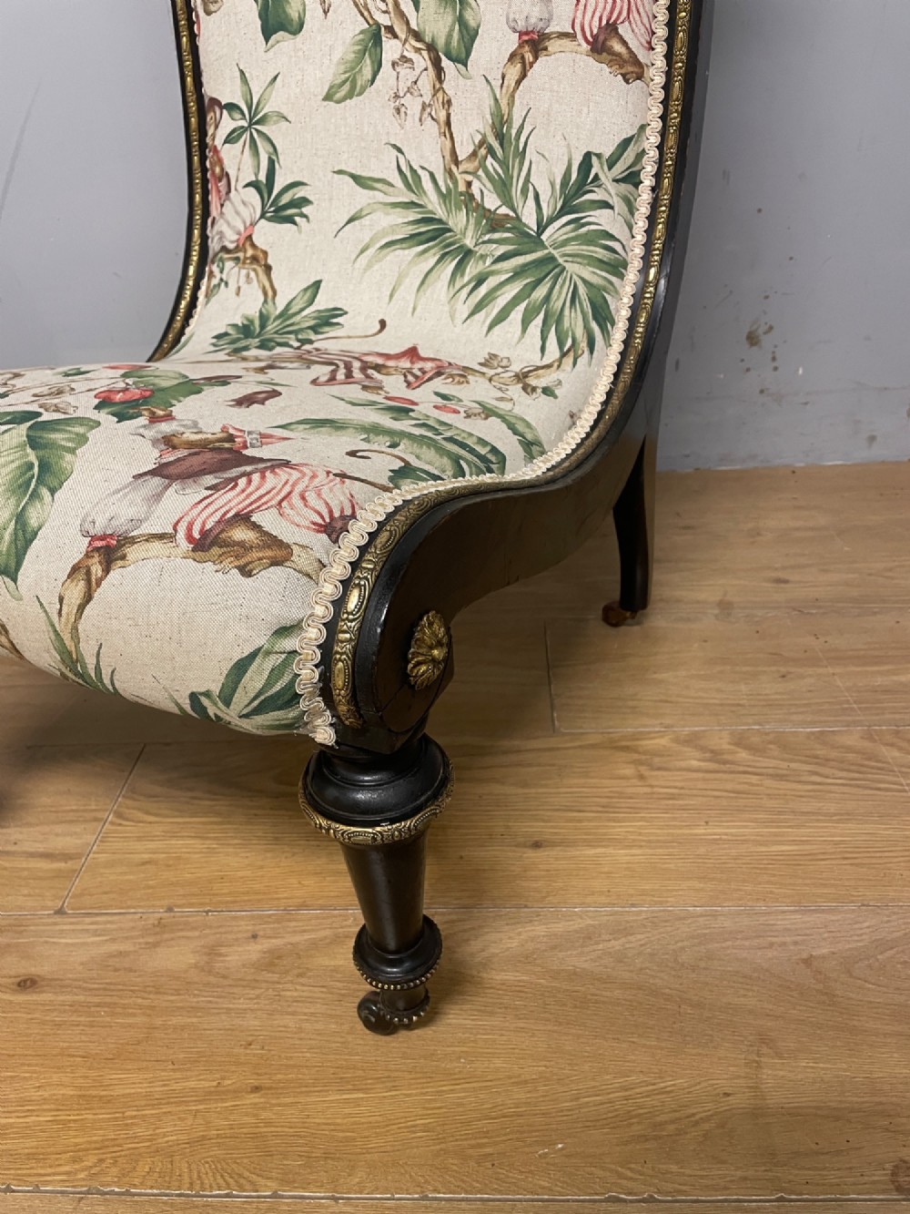 A 19th-century Aesthetic Movement slipper chair featuring an ebonised wood frame accented with gilt ormolu mounts and upholstered in botanical fabric. View II
