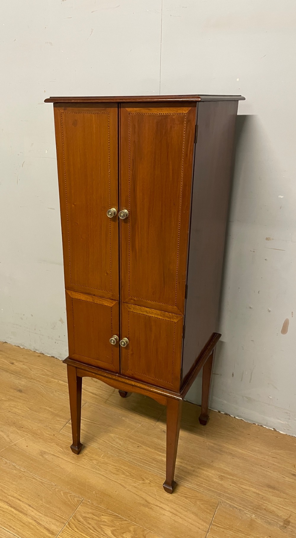 A tall slim Edwardian mahogany cabinet featuring four doors with line inlay, brass knobs, and tall tapered legs. View II