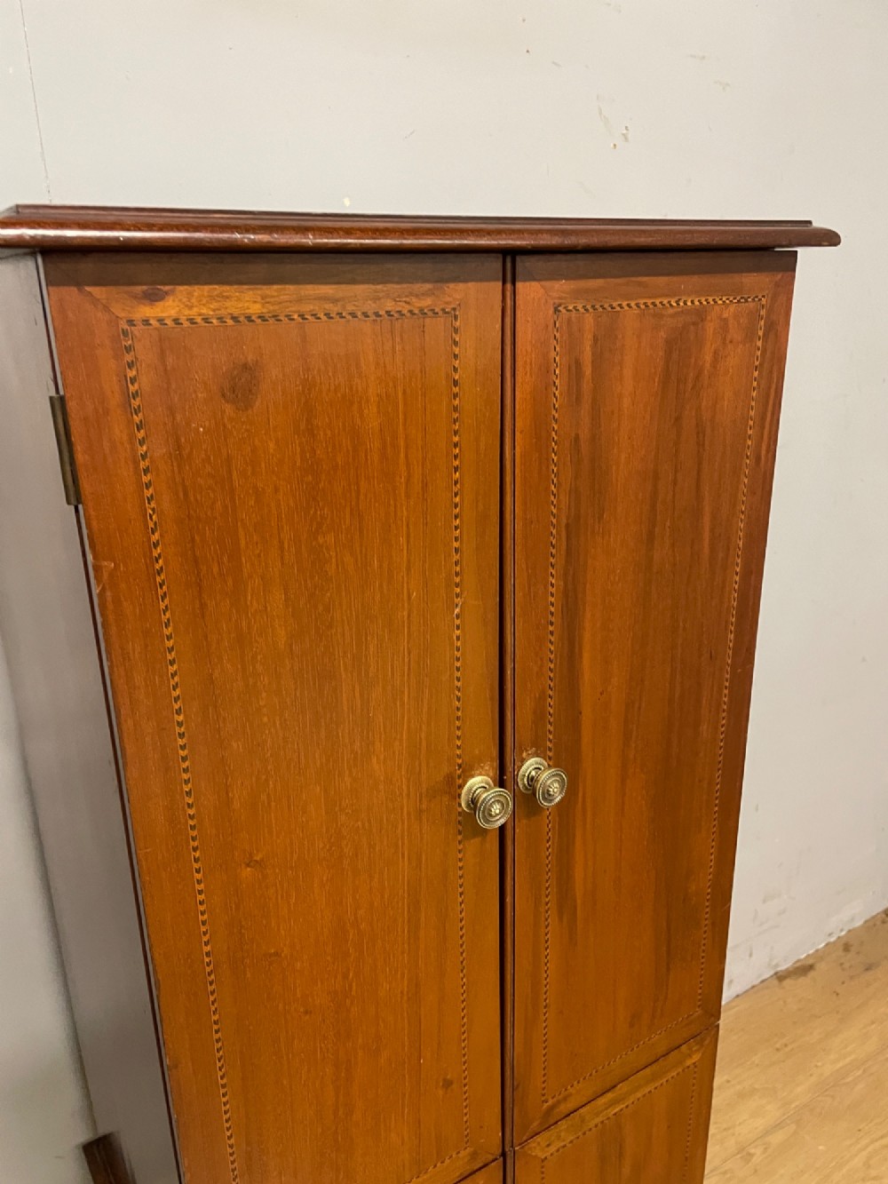 A tall slim Edwardian mahogany cabinet featuring four doors with line inlay, brass knobs, and tall tapered legs. View IV