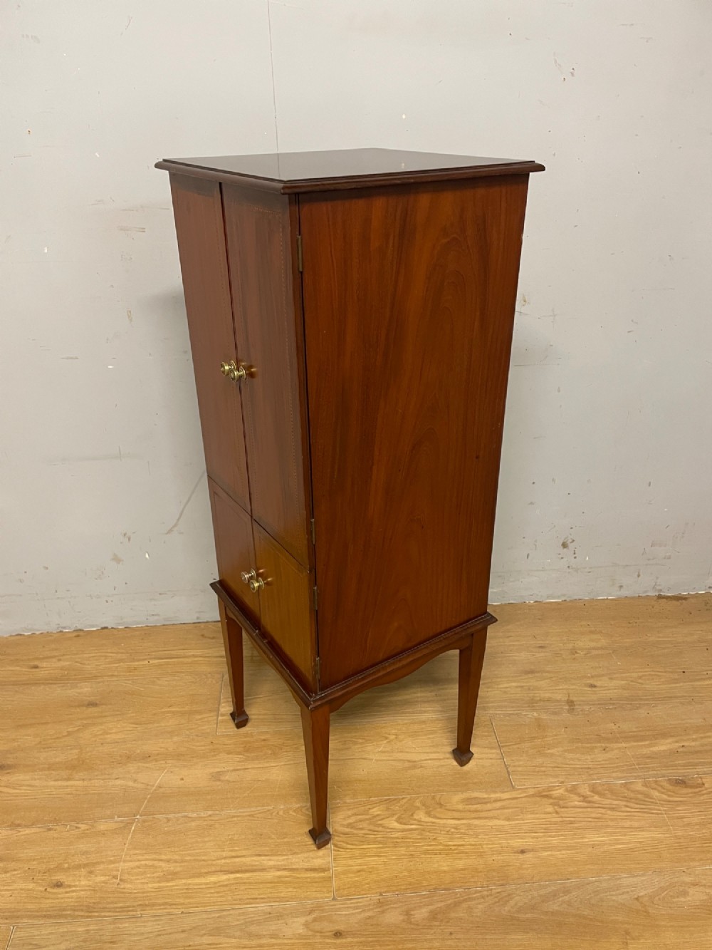 A tall slim Edwardian mahogany cabinet featuring four doors with line inlay, brass knobs, and tall tapered legs. View VII