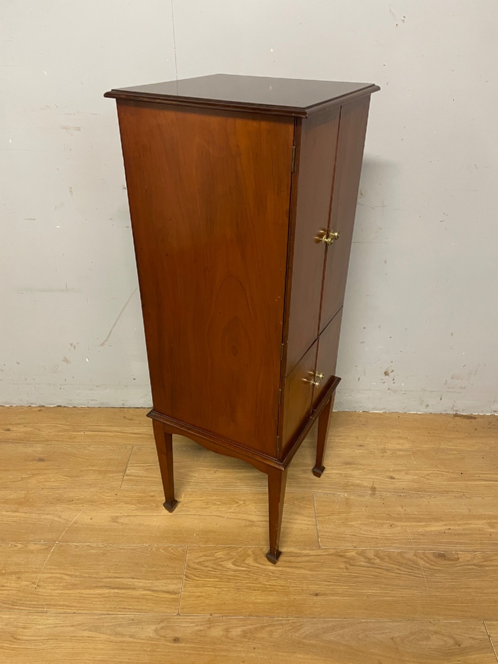 A tall slim Edwardian mahogany cabinet featuring four doors with line inlay, brass knobs, and tall tapered legs. View VIII