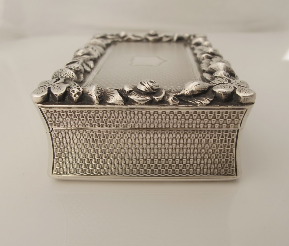A rectangular sterling silver tabletop box featuring intricate engine-turned geometric patterns, a raised floral border, and an unengraved shield cartouche in the centre. View V