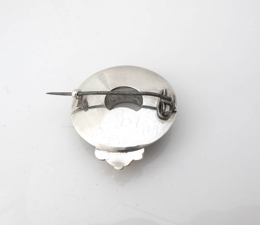 A circular Victorian Scottish silver brooch inlaid with segmented orange, green, and brown agate stones featuring an engraved silver buckle motif. View IV