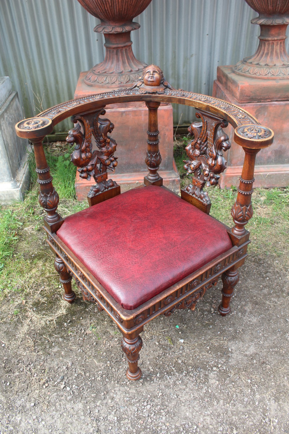 A carved dark wood corner chair featuring a red leather seat, carved splats depicting winged creatures, turned legs, and a cherub motif on the top rail.