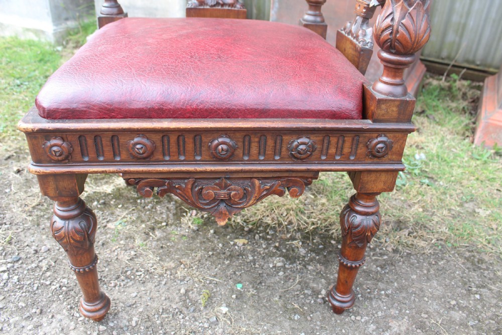 A carved dark wood corner chair featuring a red leather seat, carved splats depicting winged creatures, turned legs, and a cherub motif on the top rail. View II