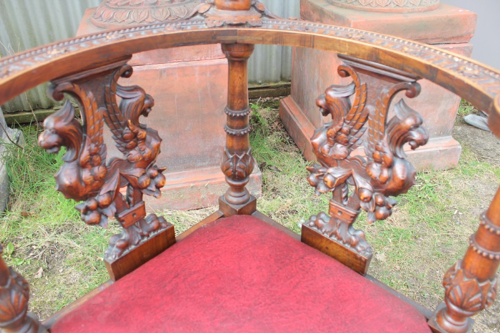 A carved dark wood corner chair featuring a red leather seat, carved splats depicting winged creatures, turned legs, and a cherub motif on the top rail. View IV