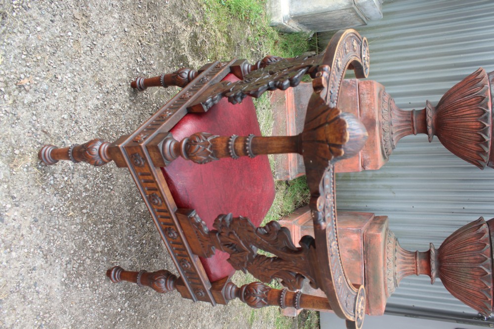 A carved dark wood corner chair featuring a red leather seat, carved splats depicting winged creatures, turned legs, and a cherub motif on the top rail. View V