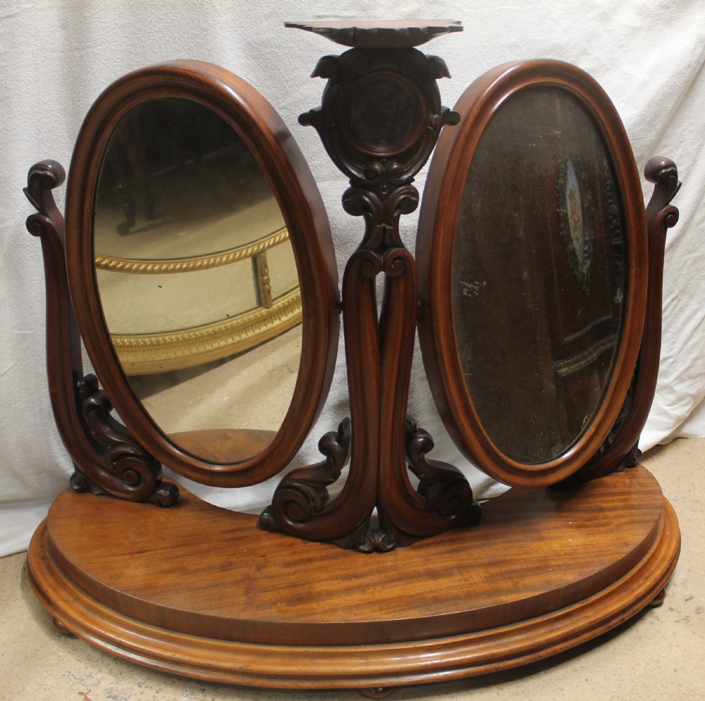 An antique Victorian carved mahogany dressing table mirror with dual oval adjustable mirrors on a central carved column and curved wooden base.
