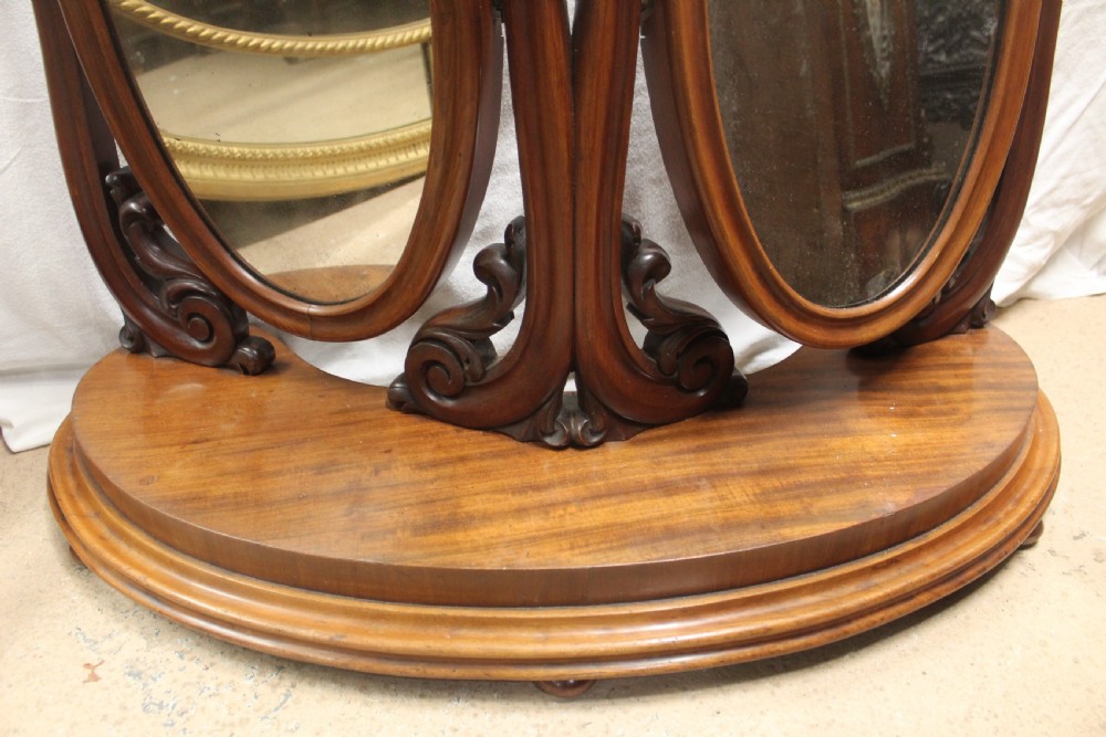 An antique Victorian carved mahogany dressing table mirror with dual oval adjustable mirrors on a central carved column and curved wooden base. View IV