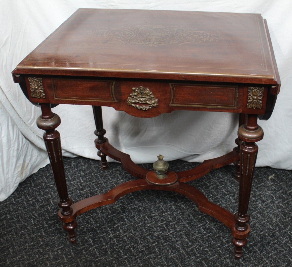 An antique French mahogany side table with brass mounts, inlaid top design, turned fluted legs, and a curved X-stretcher with a brass urn finial.