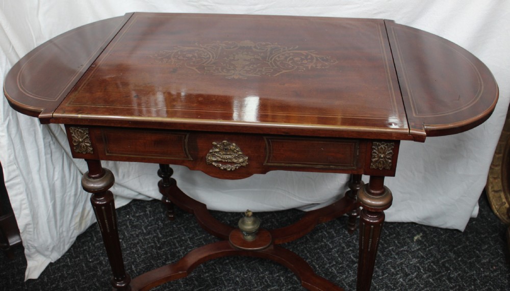 An antique French mahogany side table with brass mounts, inlaid top design, turned fluted legs, and a curved X-stretcher with a brass urn finial. View IV