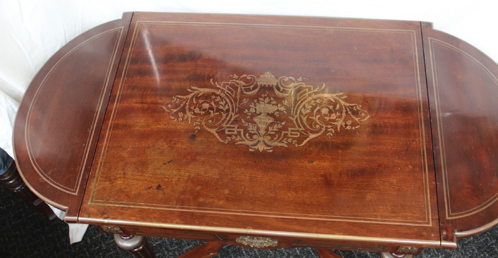 An antique French mahogany side table with brass mounts, inlaid top design, turned fluted legs, and a curved X-stretcher with a brass urn finial. View V