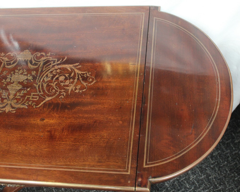 An antique French mahogany side table with brass mounts, inlaid top design, turned fluted legs, and a curved X-stretcher with a brass urn finial. View VI