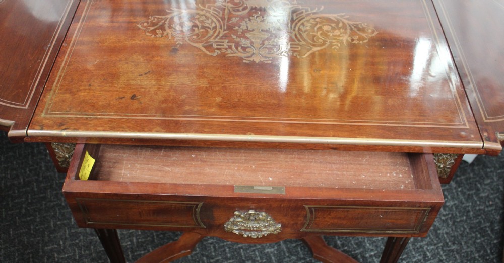 An antique French mahogany side table with brass mounts, inlaid top design, turned fluted legs, and a curved X-stretcher with a brass urn finial. View IX