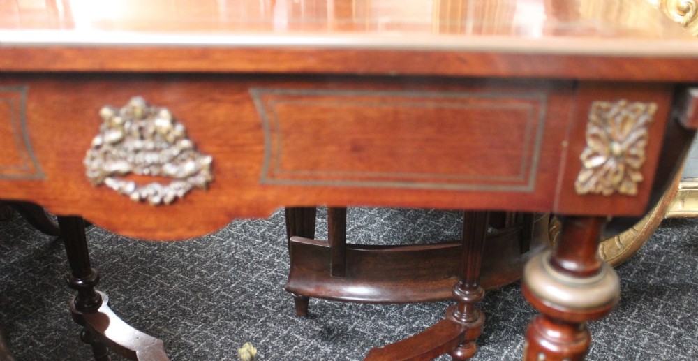 An antique French mahogany side table with brass mounts, inlaid top design, turned fluted legs, and a curved X-stretcher with a brass urn finial. View X