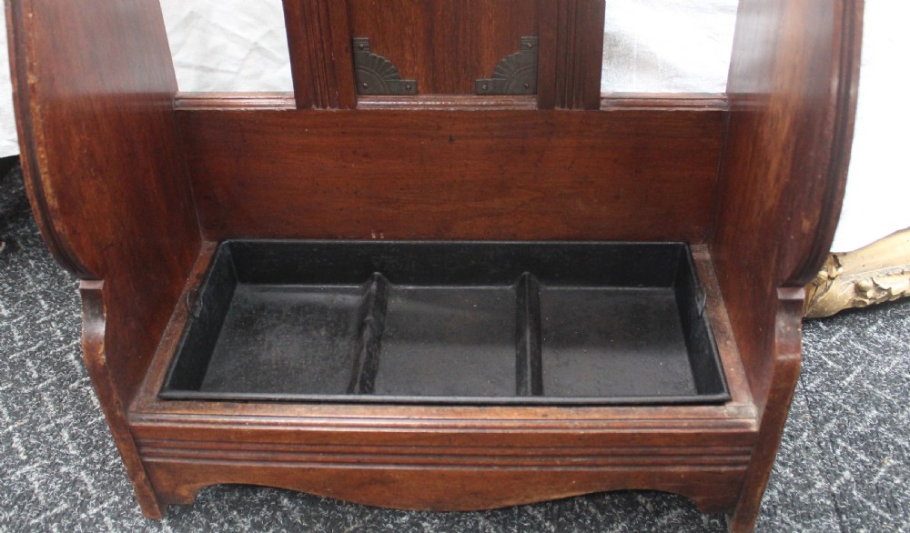 A late Victorian dark oak stick stand featuring a brass retaining bar, ceramic tile insert decorated with yellow lilies and an urn motif, and a removable black cast iron drip tray at the base. View V