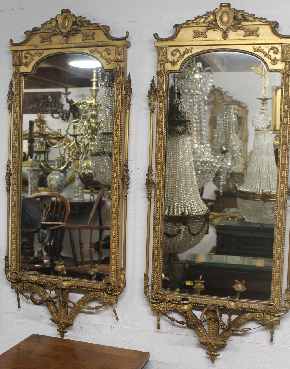 A pair of gilded Neoclassical wall mirrors featuring decorative top cresting, beaded frames, and integrated candle sconces at the base.