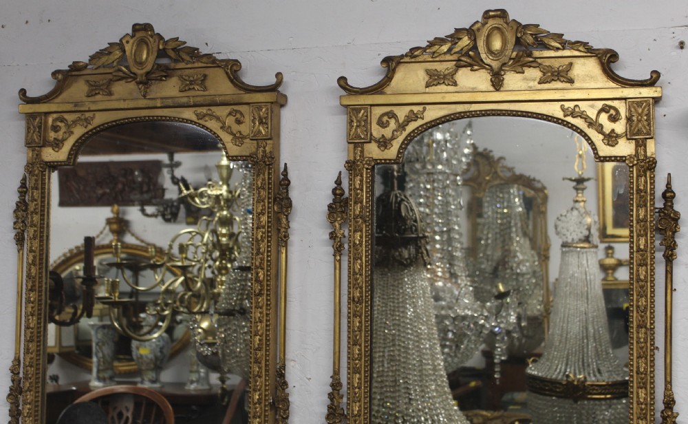 A pair of gilded Neoclassical wall mirrors featuring decorative top cresting, beaded frames, and integrated candle sconces at the base. View II
