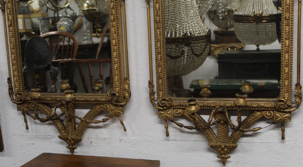 A pair of gilded Neoclassical wall mirrors featuring decorative top cresting, beaded frames, and integrated candle sconces at the base. View III