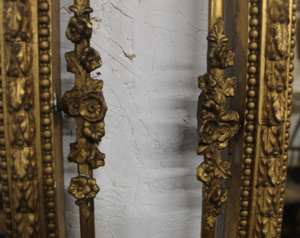 A pair of gilded Neoclassical wall mirrors featuring decorative top cresting, beaded frames, and integrated candle sconces at the base. View VI