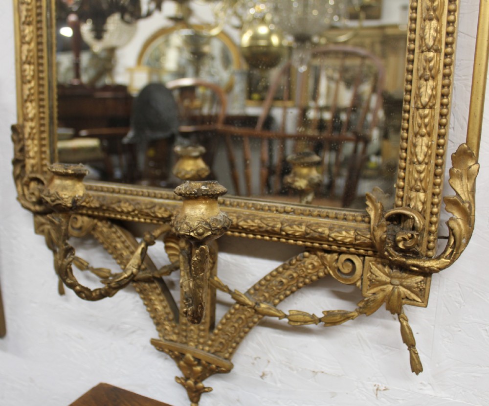 A pair of gilded Neoclassical wall mirrors featuring decorative top cresting, beaded frames, and integrated candle sconces at the base. View VII