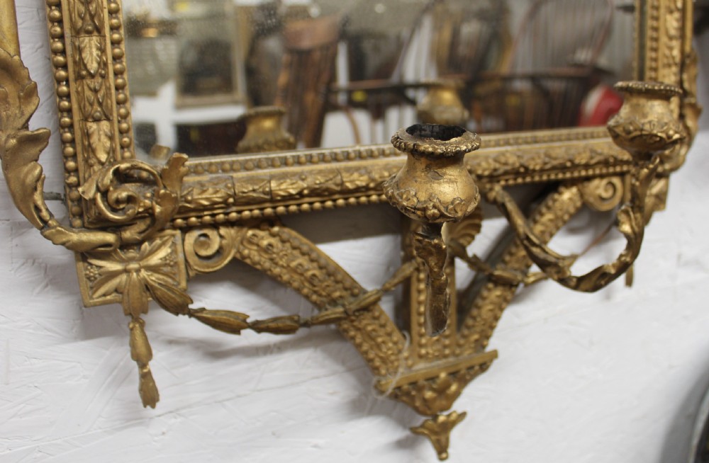 A pair of gilded Neoclassical wall mirrors featuring decorative top cresting, beaded frames, and integrated candle sconces at the base. View VIII