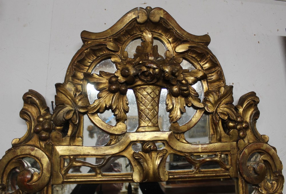 An antique carved giltwood wall mirror featuring a pierced floral basket cresting and acanthus leaf scrollwork frame. View III