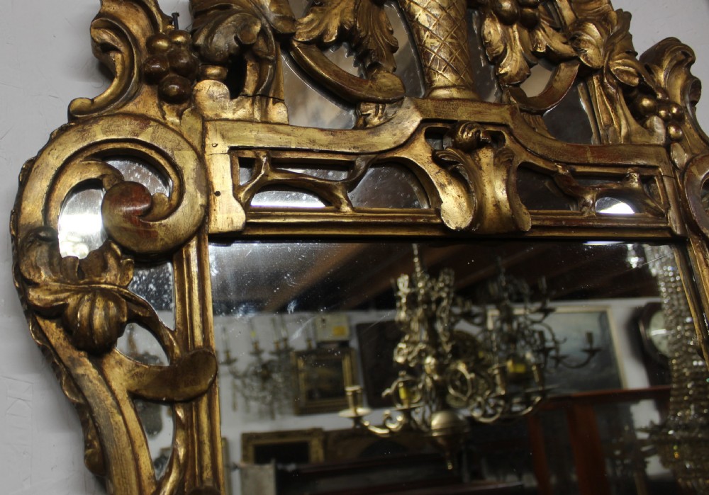 An antique carved giltwood wall mirror featuring a pierced floral basket cresting and acanthus leaf scrollwork frame. View IV