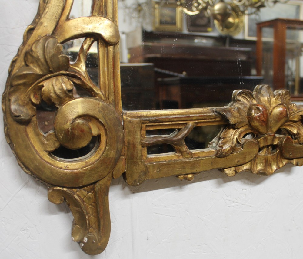An antique carved giltwood wall mirror featuring a pierced floral basket cresting and acanthus leaf scrollwork frame. View VI