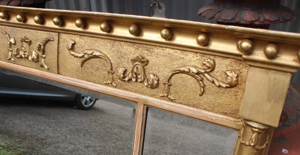 A wide gilded landscape overmantel mirror featuring three glass panels flanked by fluted columns and topped with a decorative foliate frieze. View IV
