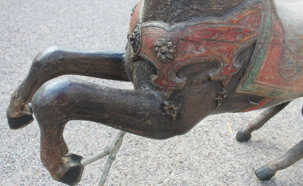 A hand-carved wooden carousel horse featuring weathered dark paint, decorative red and green saddle details, and a raised front leg pose. View VIII