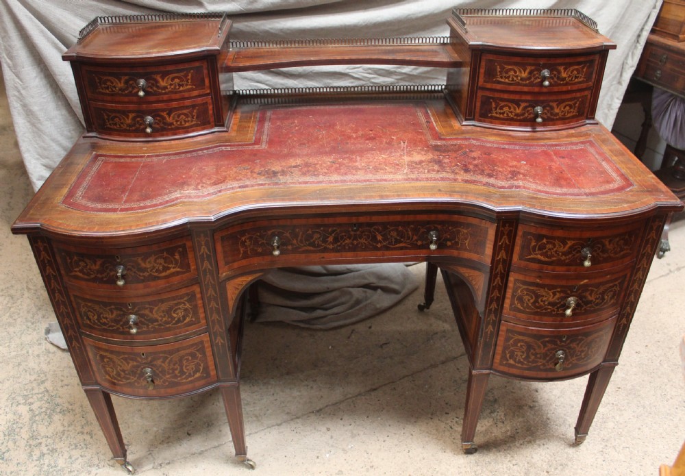 An Edwardian mahogany writing desk featuring intricate floral marquetry, a red gilt-tooled leather writing surface, a raised superstructure with drawers, and tapered legs on brass castors.