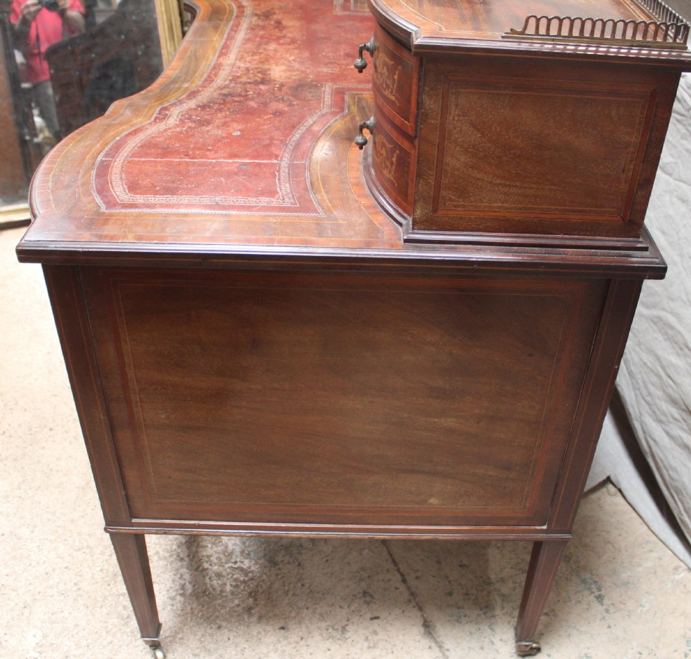 An Edwardian mahogany writing desk featuring intricate floral marquetry, a red gilt-tooled leather writing surface, a raised superstructure with drawers, and tapered legs on brass castors. View II