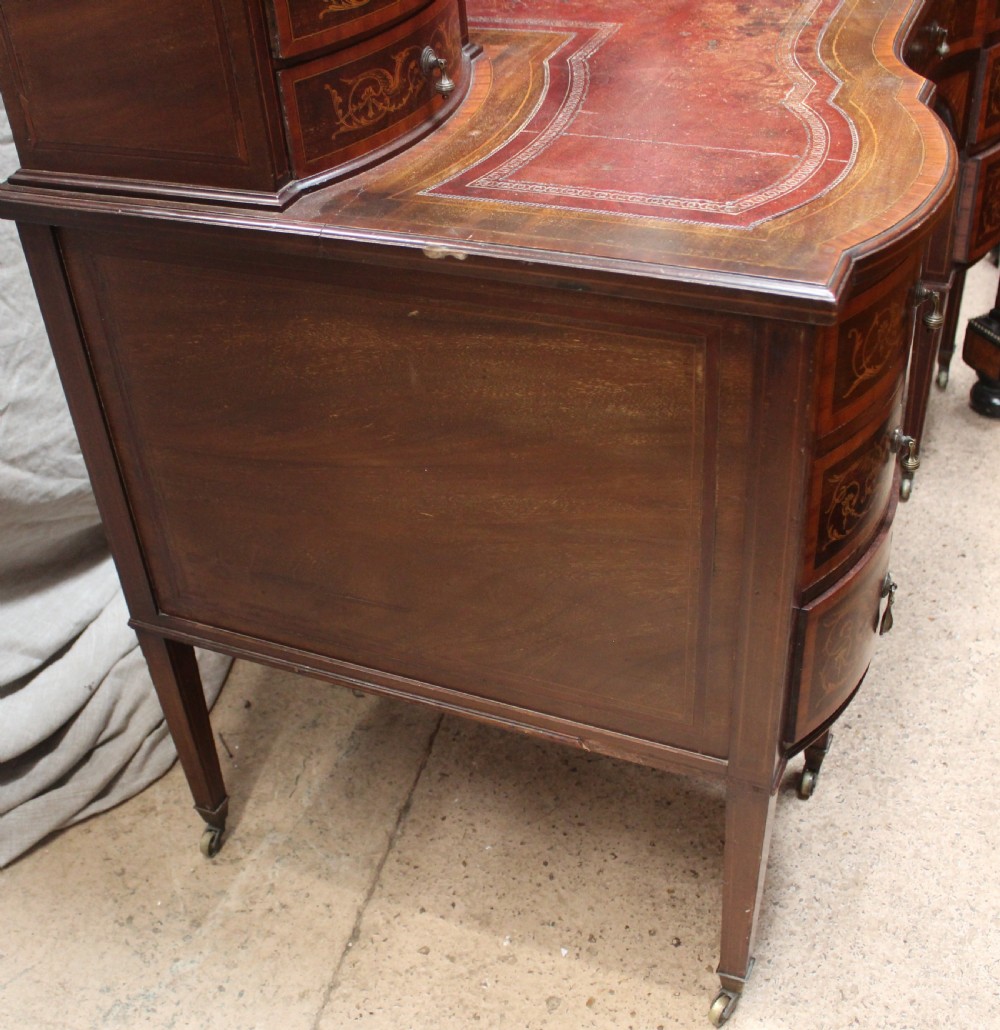 An Edwardian mahogany writing desk featuring intricate floral marquetry, a red gilt-tooled leather writing surface, a raised superstructure with drawers, and tapered legs on brass castors. View III