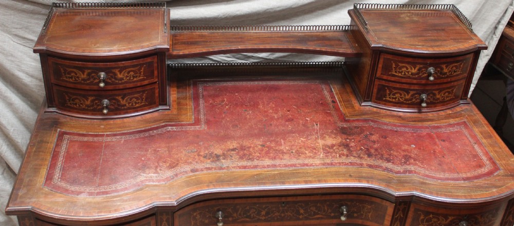 An Edwardian mahogany writing desk featuring intricate floral marquetry, a red gilt-tooled leather writing surface, a raised superstructure with drawers, and tapered legs on brass castors. View VI