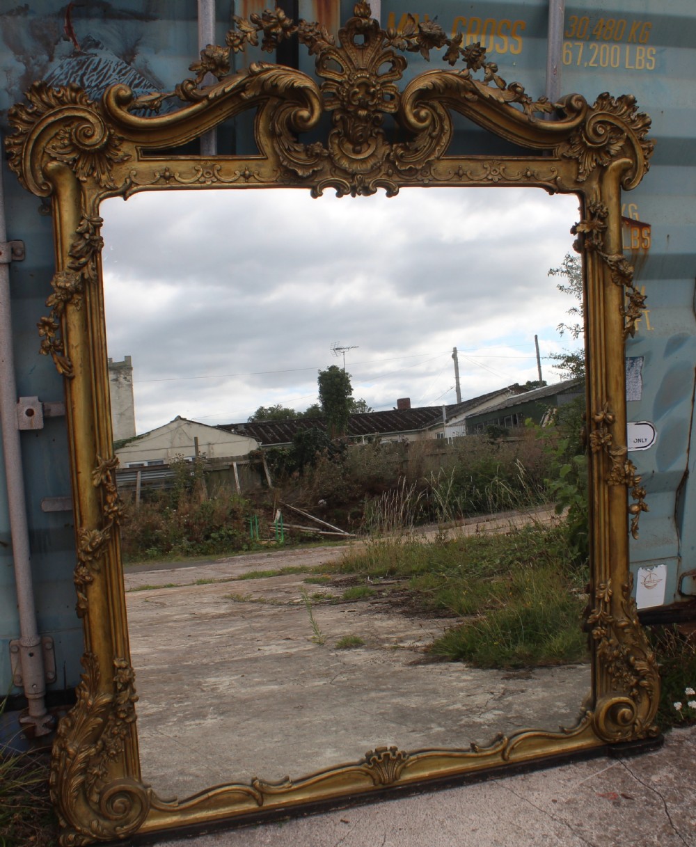A large French Rococo style overmantel mirror featuring an ornate gilded frame with detailed floral and scrollwork carvings.