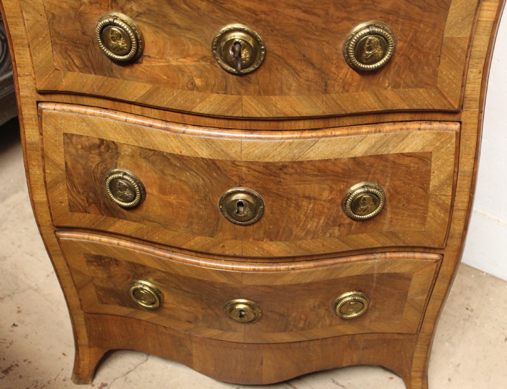 A small three-drawer walnut bombe chest of drawers featuring geometric parquetry inlay and brass ring handles. View III