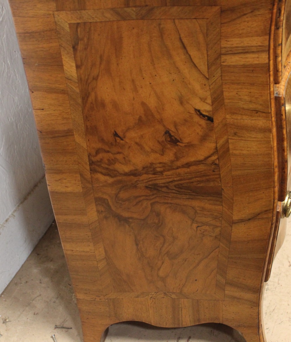 A small three-drawer walnut bombe chest of drawers featuring geometric parquetry inlay and brass ring handles. View IV