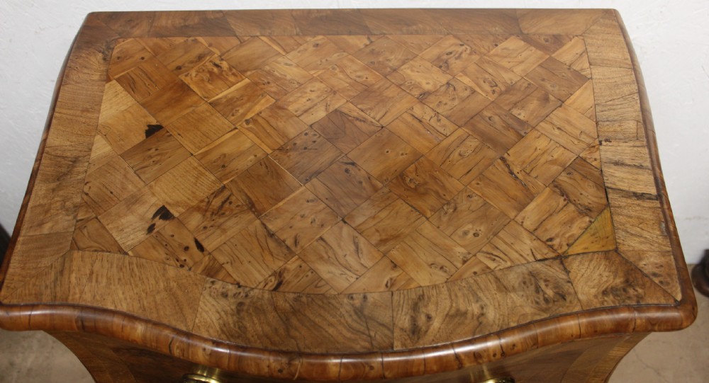 A small three-drawer walnut bombe chest of drawers featuring geometric parquetry inlay and brass ring handles. View V