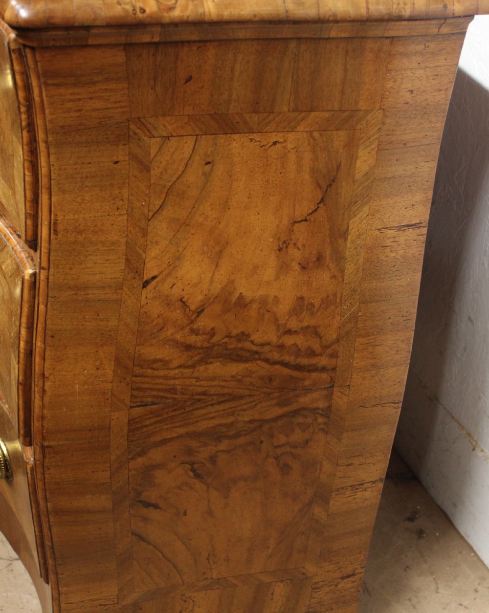 A small three-drawer walnut bombe chest of drawers featuring geometric parquetry inlay and brass ring handles. View VI
