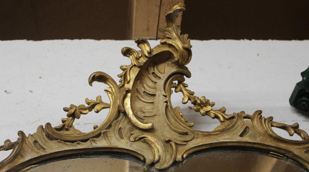 An antique French Rococo wall mirror featuring a gilded wood frame carved with leaf cresting, scrolled edges, and foliate details. View III