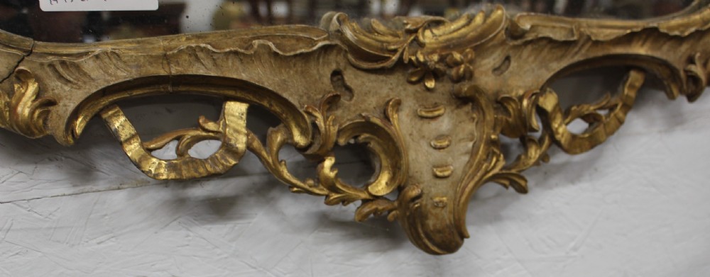 An antique French Rococo wall mirror featuring a gilded wood frame carved with leaf cresting, scrolled edges, and foliate details. View IV