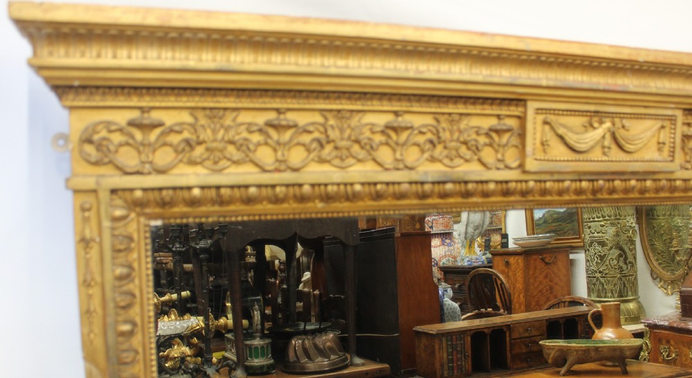 A large rectangular gilded overmantel mirror featuring a moulded frame with floral swags, a guilloche frieze, and decorative plinth bases. View II